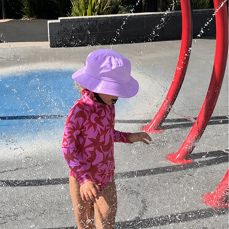 Child wearing bucket hat lilac waterproof on the splash park 