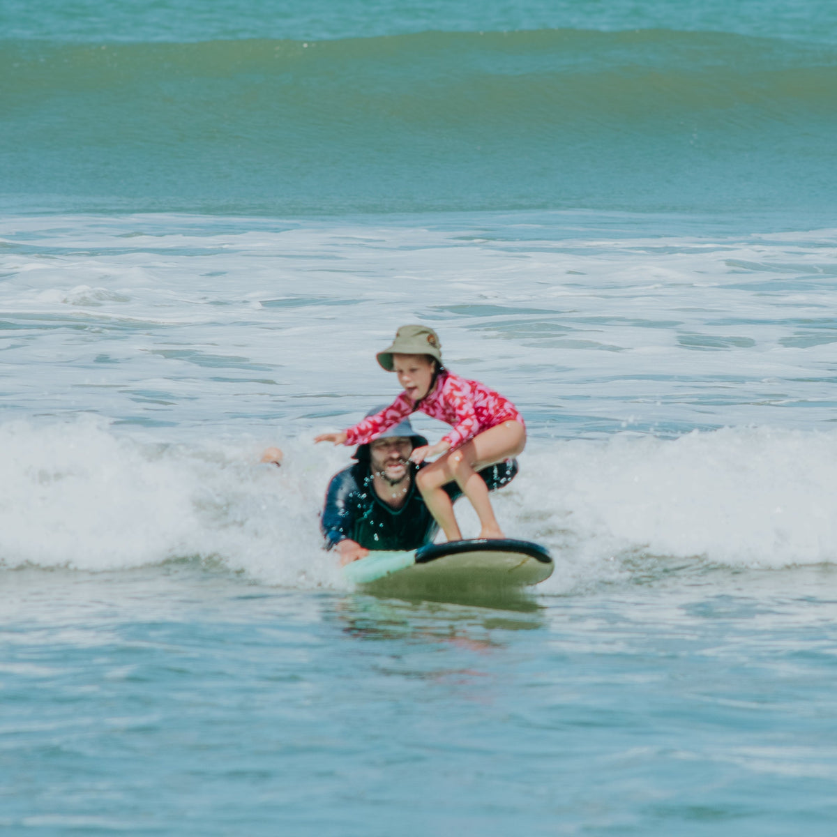 Kid learning how to surf wearing a surf hat on a foamie board at the beach