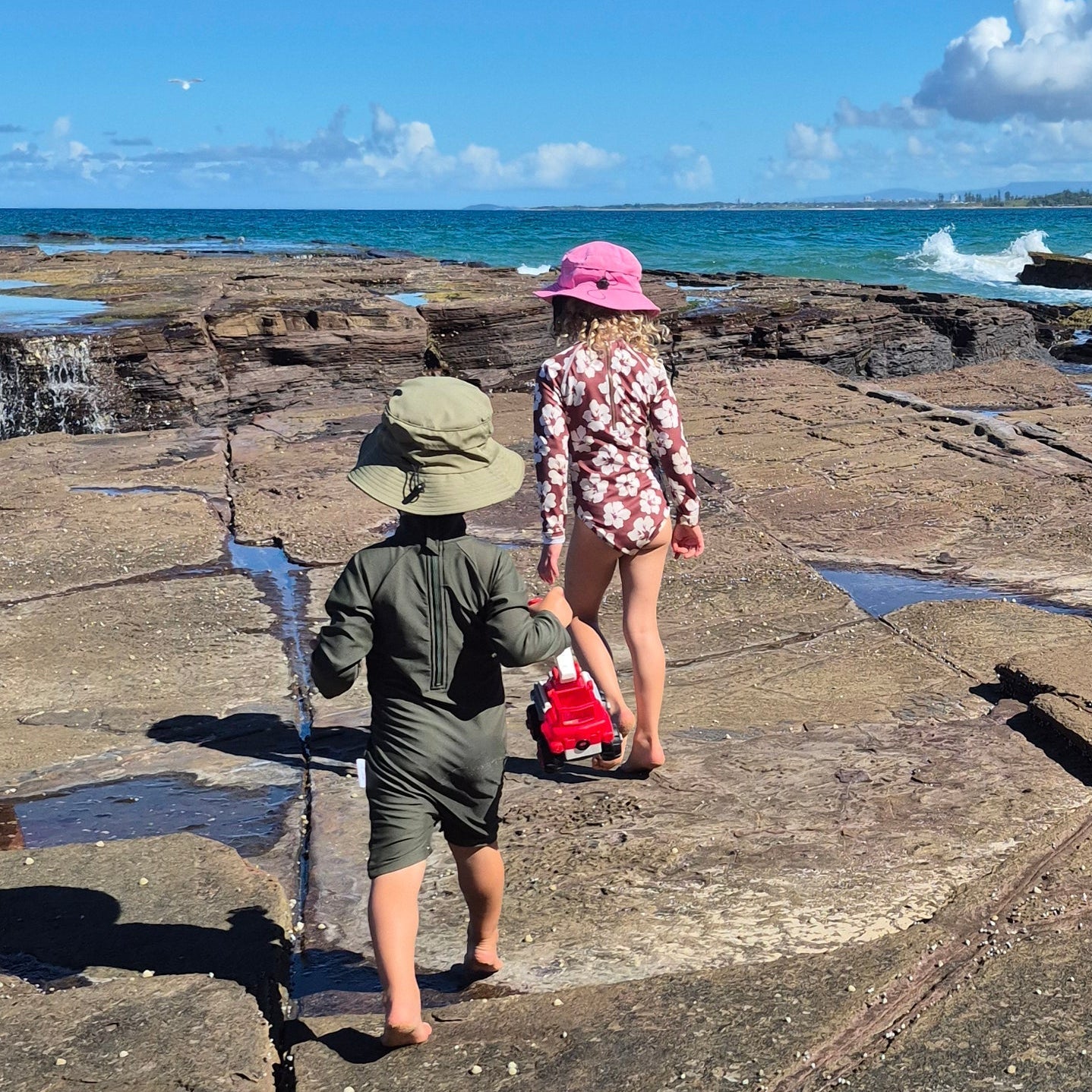 Two children playing on a rocky shoreline with ocean and sky in the background