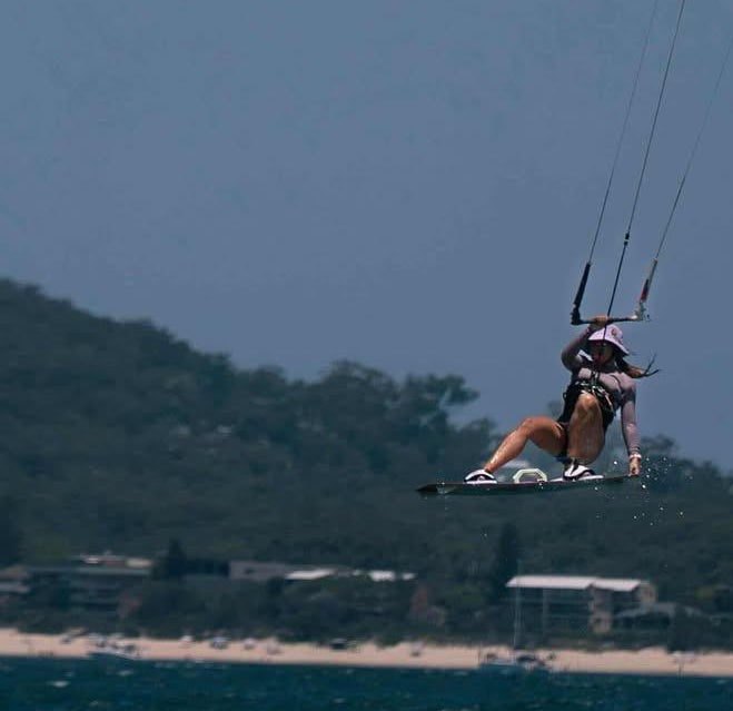 Kitesurfer wearing a sun hat helmet head protection in lilac while doing a kitesurfing jump on water