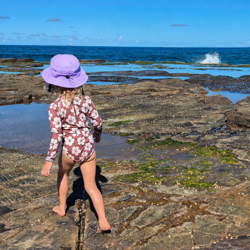 Child in a purple hat walking on rocky tidal flats with ocean in the background