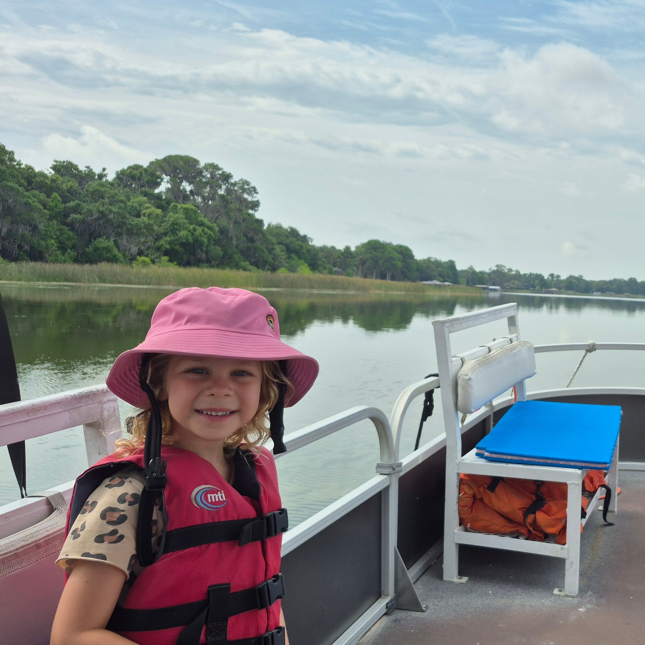 Child on a boat deck with a lake and trees in the background wearing a bucket hat lightweight and quick dry 