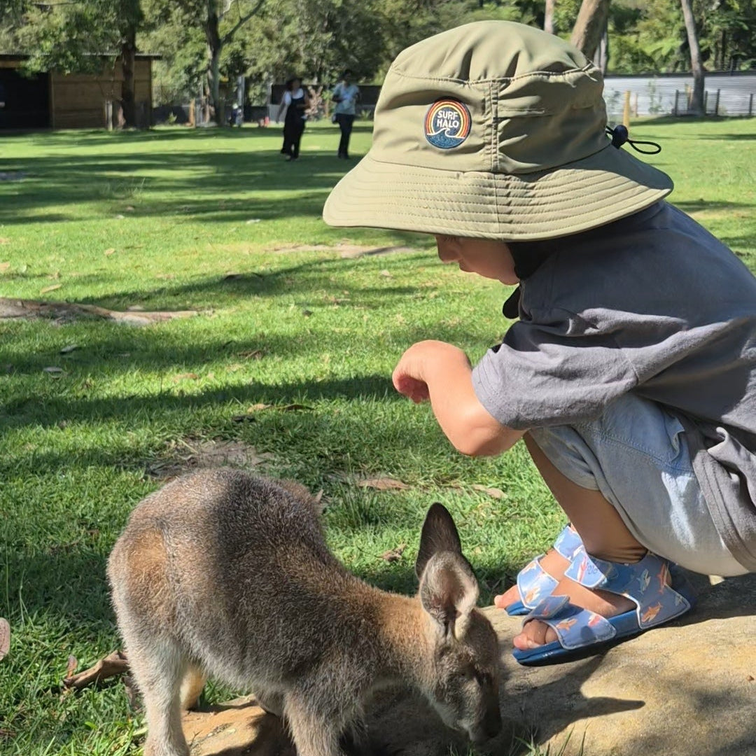 Toddler laying with a kangaroo wearing a surf hat helmet  