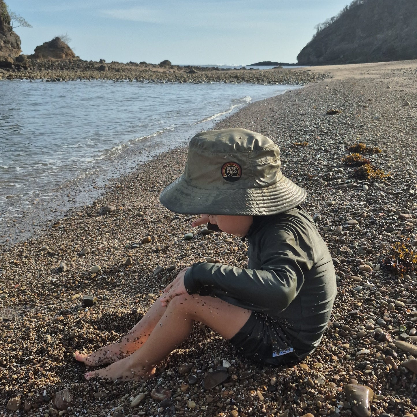 child at the beach wearing olive green surf hat 